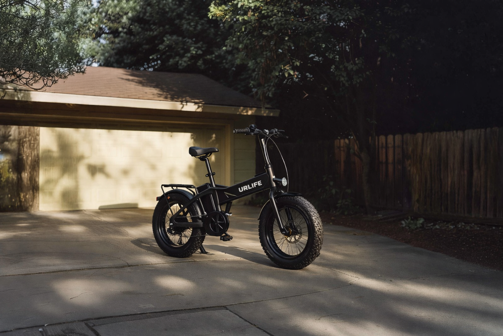 Black electric bike parked on a driveway with trees and a house in the background